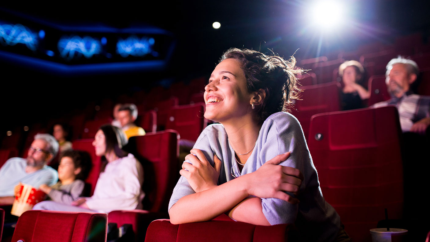 Smiling movie goes sit in a theatre looking toward the screen.